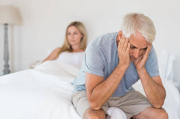 Frustrated man sitting apart from his partner at home, a common sign of reduced libido and low male drive with age
